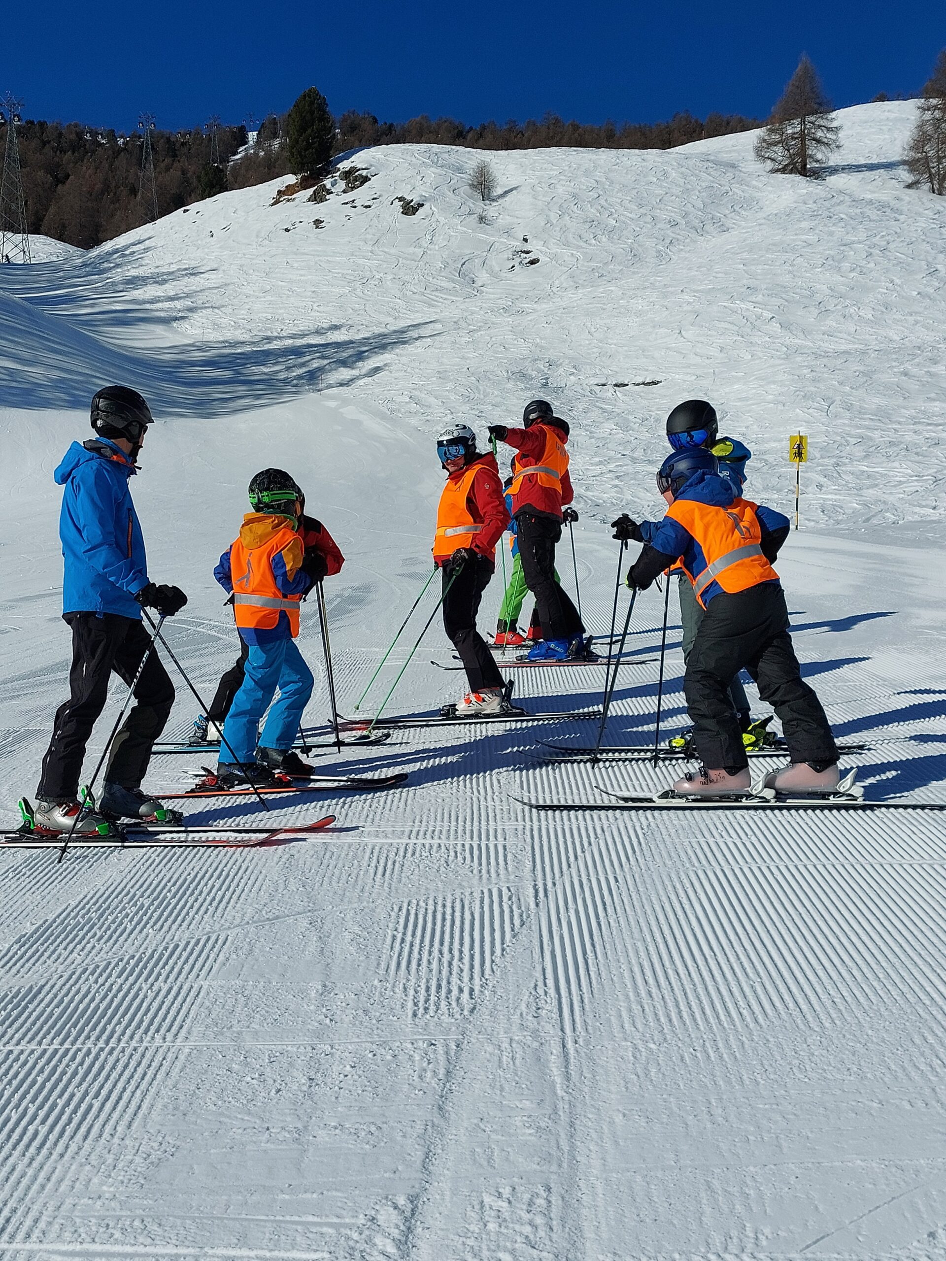 Schülerinnen und Schüler mit Begleitpersonen auf der Skipiste bei strahlendem Sonnenschein.